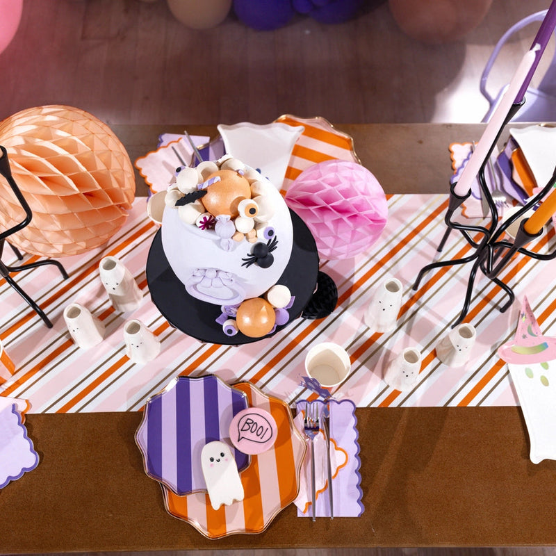 Overhead pastel Halloween table with striped runner and layered purple and orange striped dinner plates.