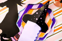 Detail of witch’s hat napkin holder with lilac guest towel tucked through the slit on layered purple and orange plates.