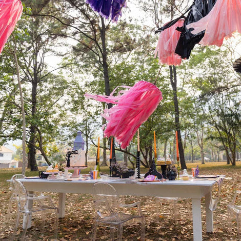 Outdoor Halloween table with tassel garlands, striped runner, and place settings styled with witch’s hat napkin holders.