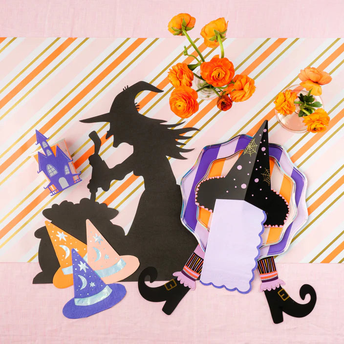 Overhead pastel Halloween scene with orange flowers, layered plates, and two witch’s hat napkin holders used as place cards.