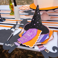 Close place setting on witch placemat with layered striped plates and a witch’s hat napkin holder over a purple guest towel.