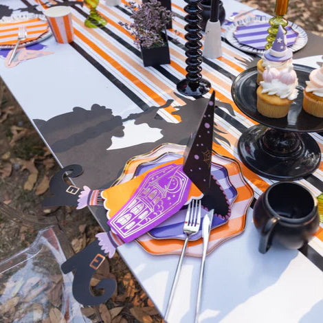 Long table view with striped runner, cupcakes, and multiple witch’s hat napkin holders at each plate.