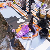 Long table view with striped runner, cupcakes, and multiple witch’s hat napkin holders at each plate.