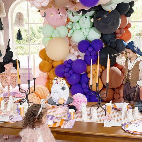 Children in costume at a pastel Halloween table set with witch hat napkins and striped runner.
