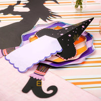 Angle view of layered plates on pink striped runner with orange flowers and witch’s legs accents tucked under the setting.