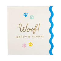 Product image of Woof Happy Birthday cocktail napkin with paw prints and blue scallop edge.