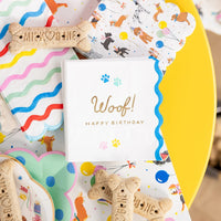 Overhead close up of Woof napkin surrounded by dog bone treats and party paper goods.