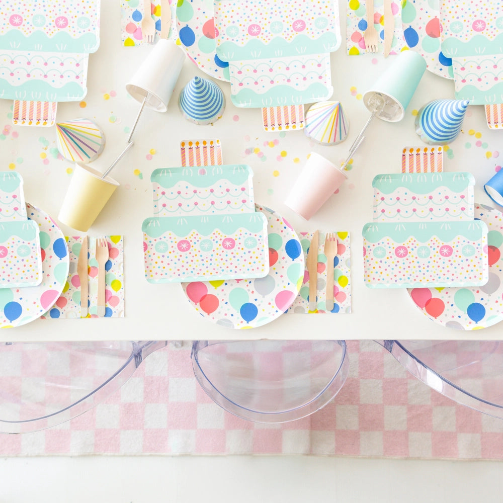 Overhead party table styled with balloon napkins under wooden utensils alongside cake-shaped and balloon plates	