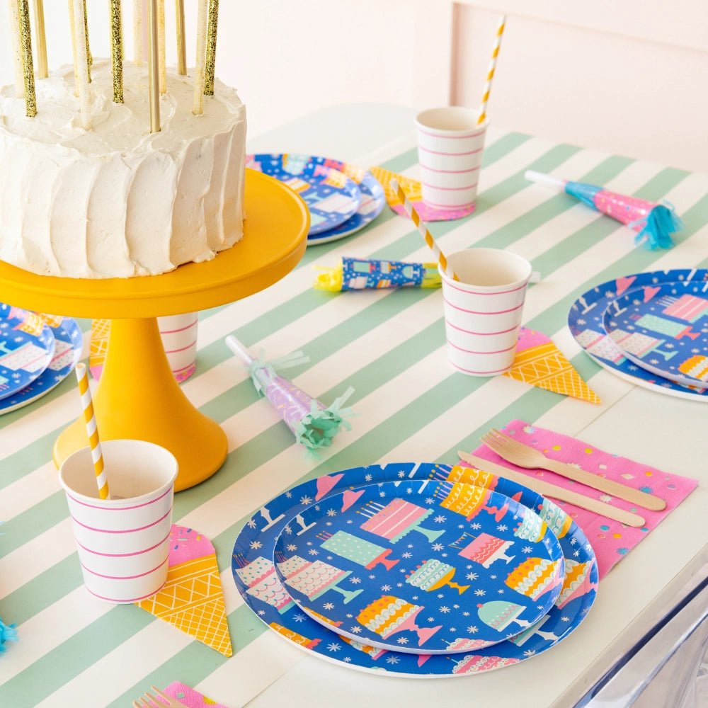 Birthday table with yellow cake stand, green-striped runner, blue cake-print plates, ice-cream cone napkins, and cups