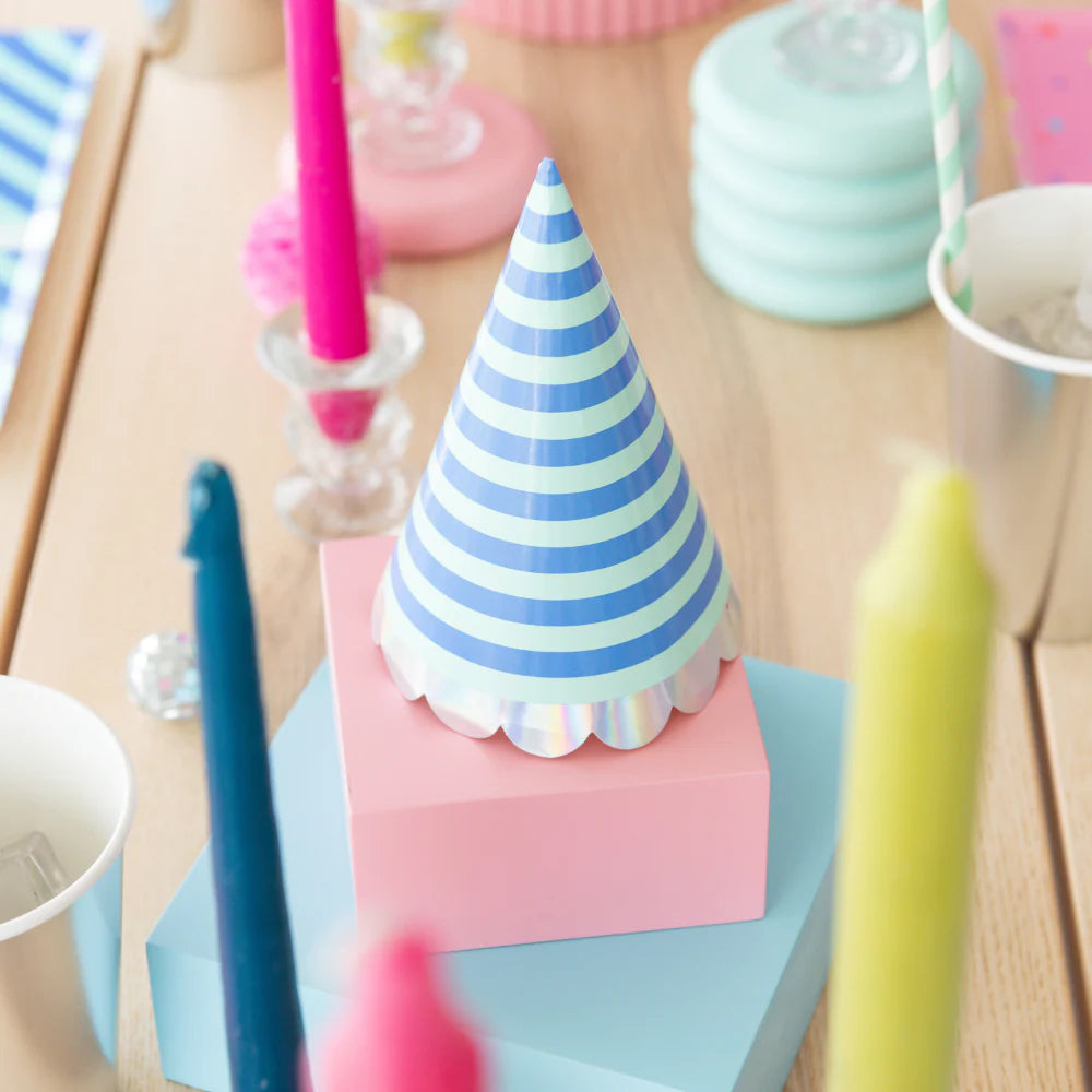 Blue striped cone party hat with iridescent scallop trim displayed on pastel boxes among colorful birthday table décor	