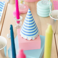Blue striped cone party hat with iridescent scallop trim displayed on pastel boxes among colorful birthday table décor	