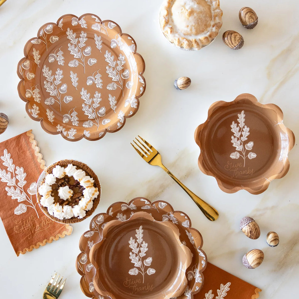 Fall tablescape with acorn plates, napkins, gold flatware, and pies