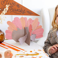 Child smiling next to assembled turkey with Give Thanks pennant