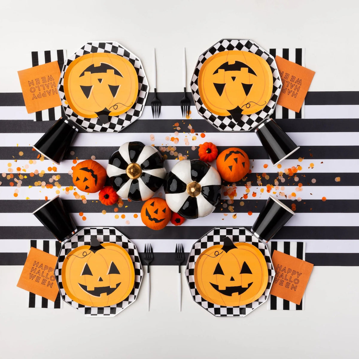 Overhead tablescape with checkerboard chargers and jack-o-lantern pumpkin paper plates, bold Halloween plates look