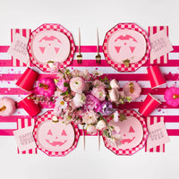Overhead tablescape with pink jack o lantern pumpkin paper plates, flowers, and stripes, cute pink halloween decor