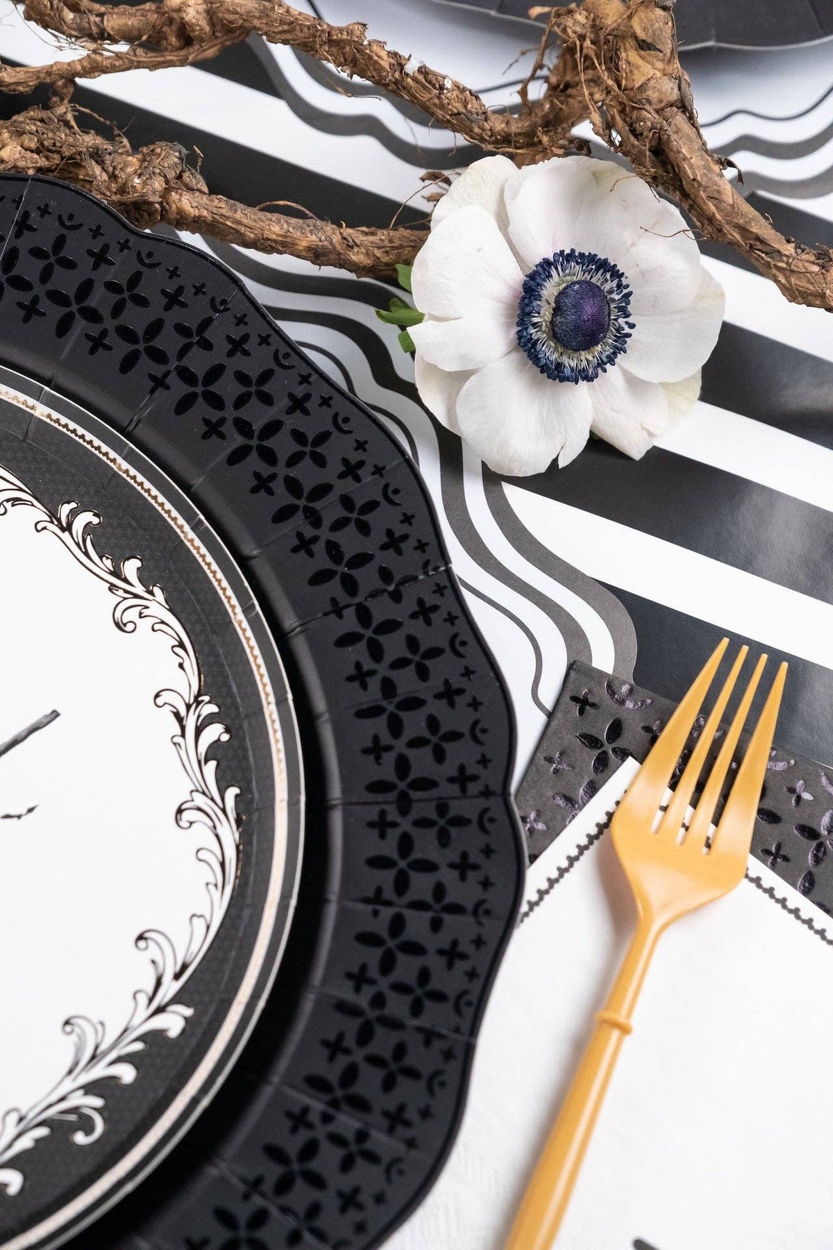 Styled gothic table setting with a white anemone flower resting next to a black die-cut paper plate and gold fork.