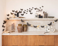 Close up styled view of the pre-strung moths and stars garland styled on a mantel next to dark taper candles, ceramic jars, and 3D fluttering moth wall decals.