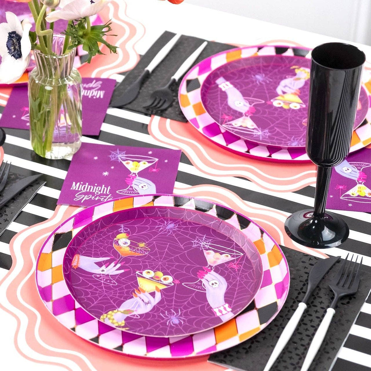 Angled shot of a moody Halloween tablescape anchored by the purple dessert plates, black cups, and white floral centerpieces.