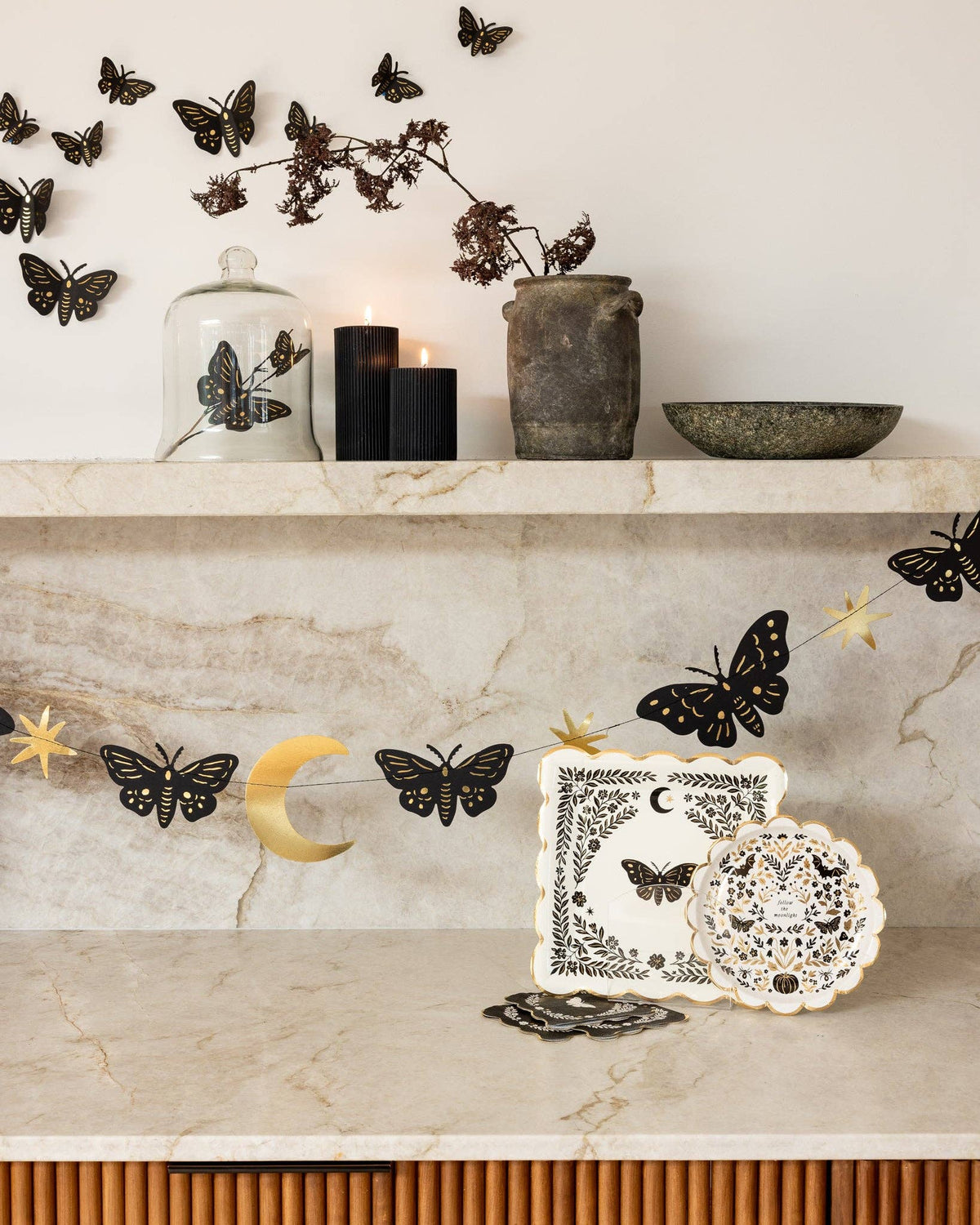 Moonlight collection marble shelf with the folk-art plate propped beside the moth napkin, black gold-foil moth wall decor swarming above, candles, and a gold crescent moon.