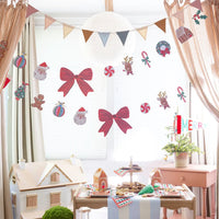 Kids' Christmas party table set with gingham plates under Christmas icon garlands; garlands, pennant, and treat boxes shown separately, not included
