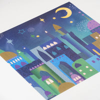 Colorful paper placemat with a cityscape design featuring buildings, stars, and a moon on a white background.