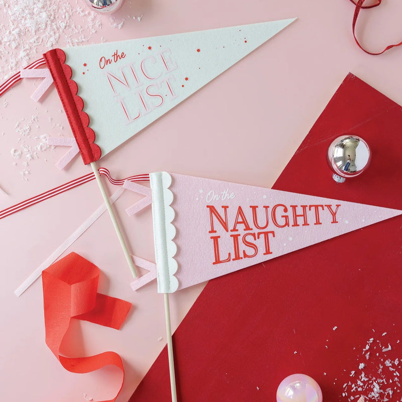 Styled scene with Naughty and Nice felt Christmas pennant banners, ornaments, and ribbon—tabletop flatlay.