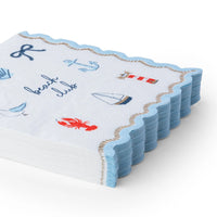 Stack of nautical beach club cocktail napkins with navy nautical icons, a red lobster and lighthouse, and a light blue scalloped gold rope edge.