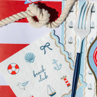 Nautical sailboat guest towel styled with blue and gold cutlery, a rope knot, and a coordinating beach club napkin.