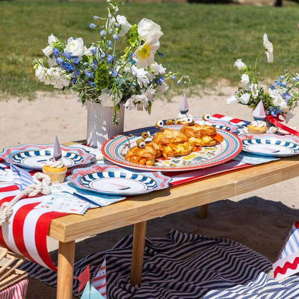 Nautical beach party table with sailboat guest towels, striped sailboat plates, sailboat cupcake toppers, and a red-and-white stripe runner.