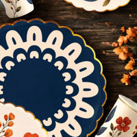 Navy doily dinner plate on a wood table with floral party cups and dried orange flowers
