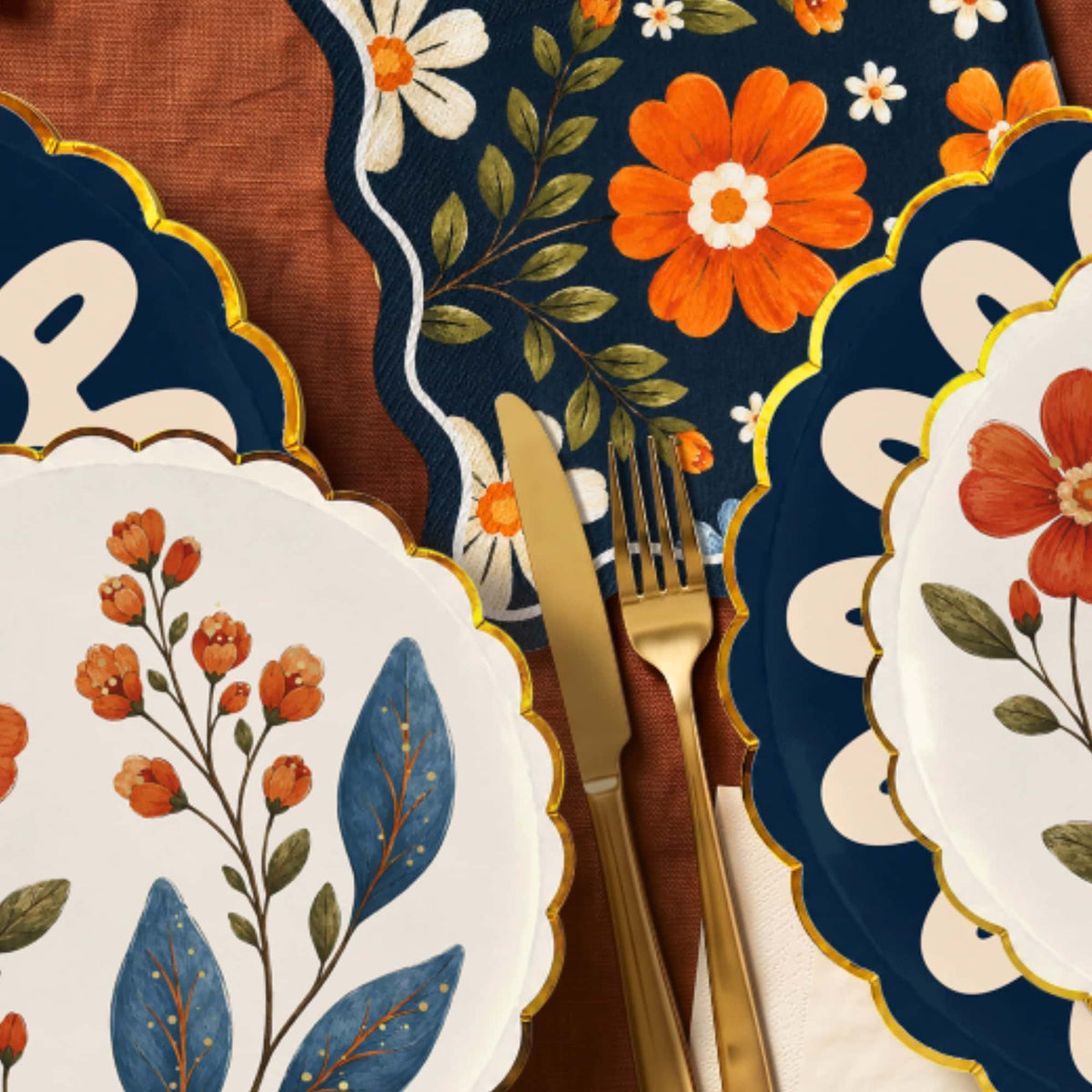 Navy floral napkin beside gold flatware under scalloped wildflower and navy doily plates on rust linen
