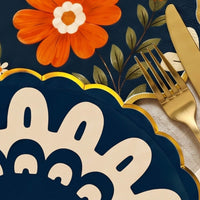 Close-up of the gold scalloped rim on a navy doily plate beside gold flatware and a navy floral napkin