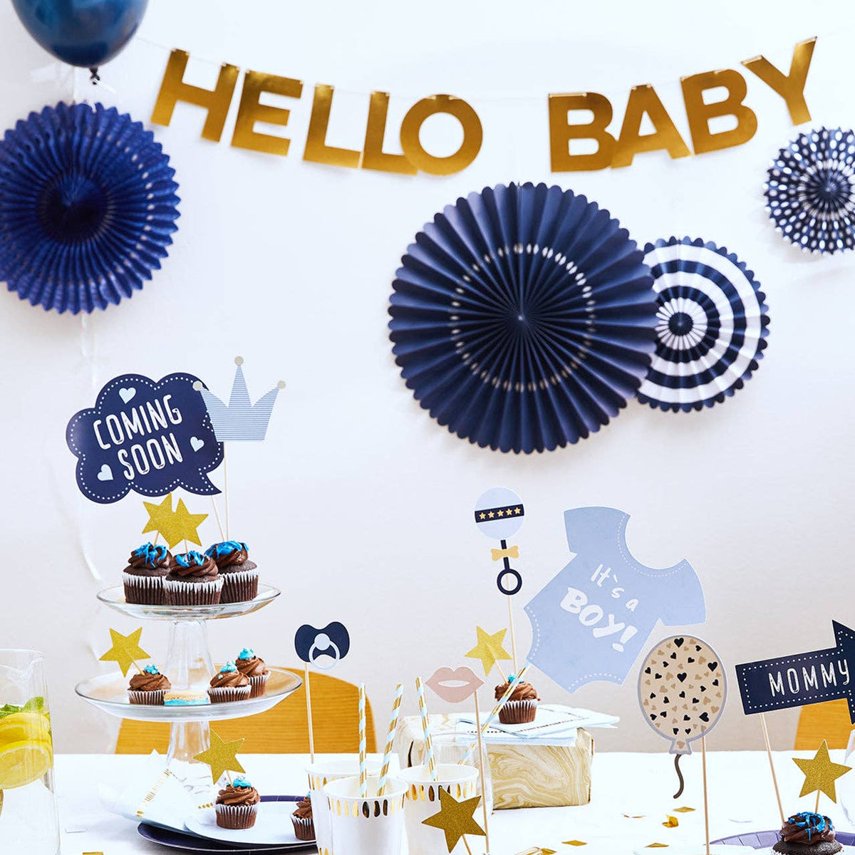 Classic navy and gold baby shower backdrop with navy party fans, "Hello Baby" banner, and "It's a Boy" cupcake display.