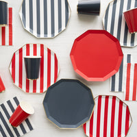  Red, navy, and cabana stripe paper plates with matching paper cups and red and navy striped guest towel napkins on a white wood surface