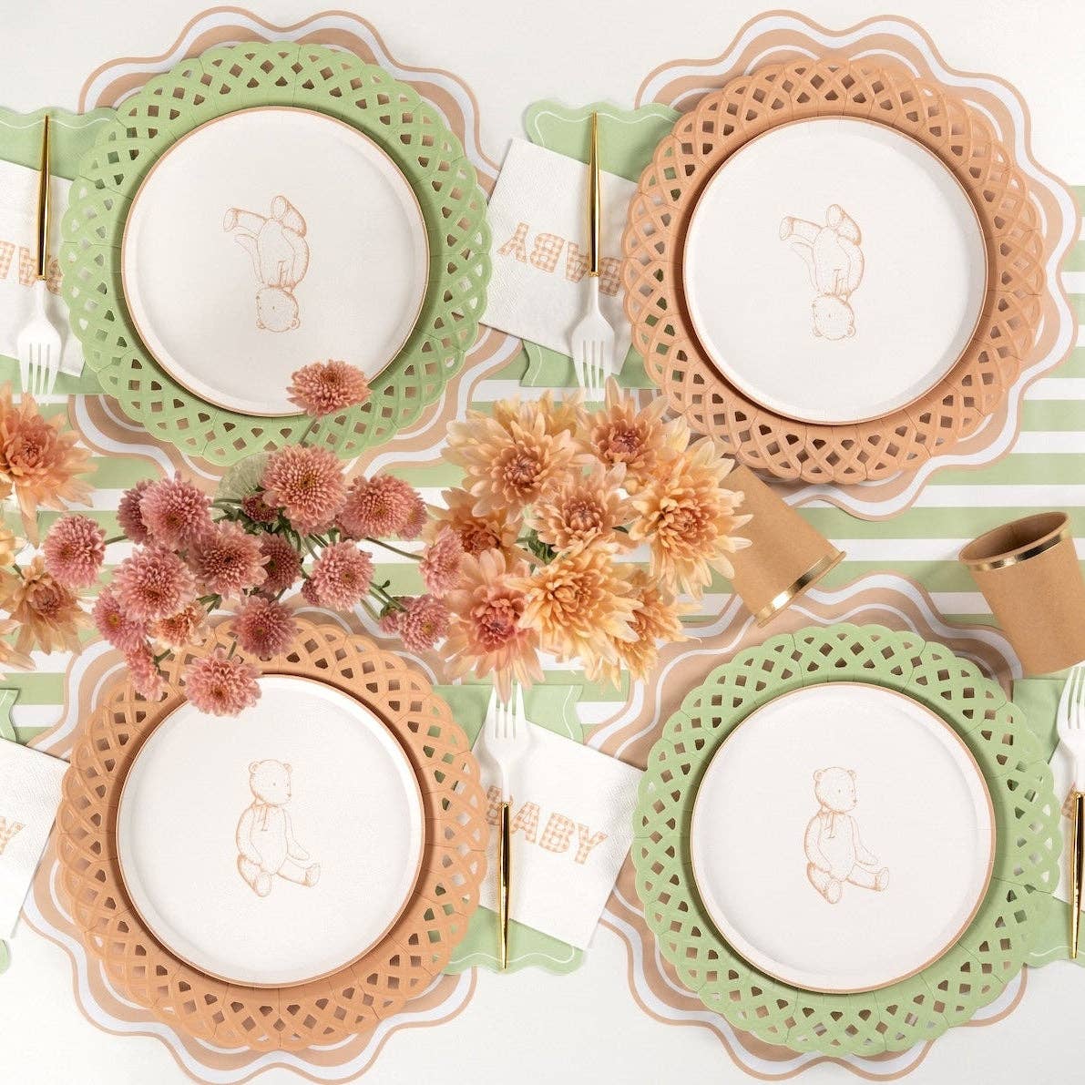 Neutral baby shower tablescape showing light brown and sage green basketweave paper plates layered with a white embroidered baby napkin.