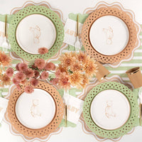 Neutral baby shower tablescape showing light brown and sage green basketweave paper plates layered with a white embroidered baby napkin.