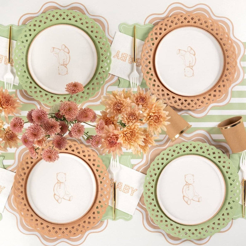 Neutral baby shower tablescape showing light brown and sage green basketweave paper plates layered with a white embroidered baby napkin.