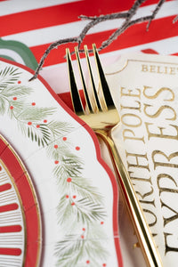 Detail of a North Pole Express plate and place card on the wreath dinner plate with evergreen sprigs and a gold fork.