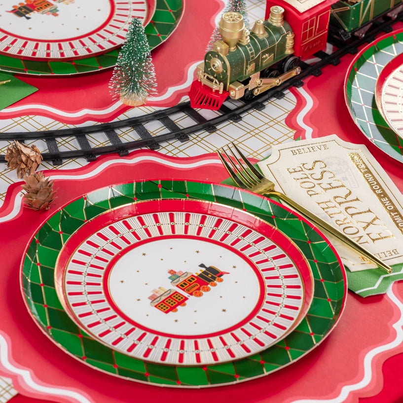 Tablescape with train track and green/red plates beside ticket napkin