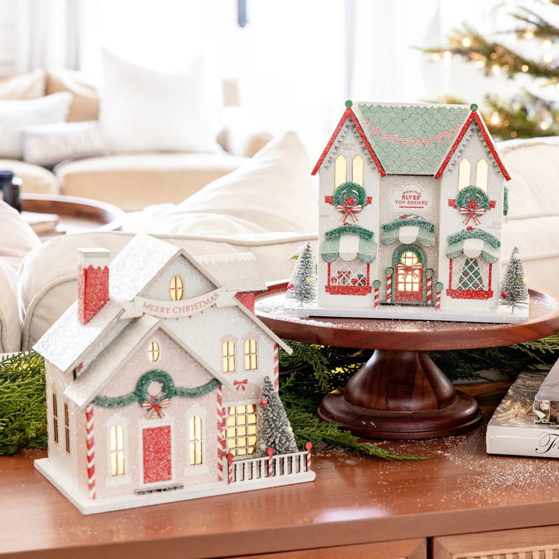 Collection of three Christmas village houses on a coffee table with a tree, including the Santa's House village piece.