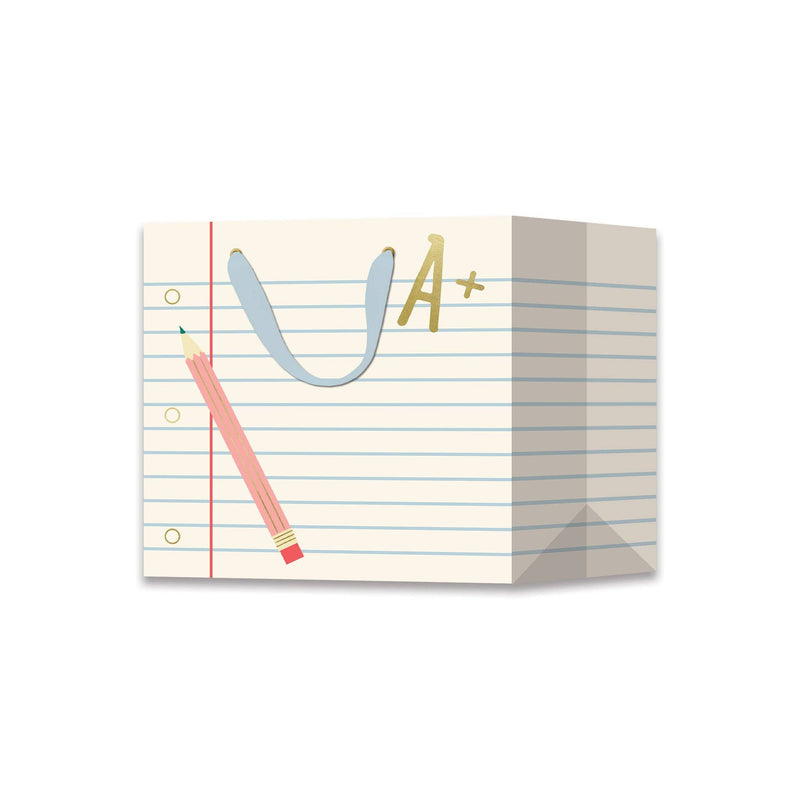 Notebook paper favor bag printed like ruled loose-leaf paper with a red margin, gold binder holes, a pink pencil, a gold foil "A+," and light blue ribbon handles.