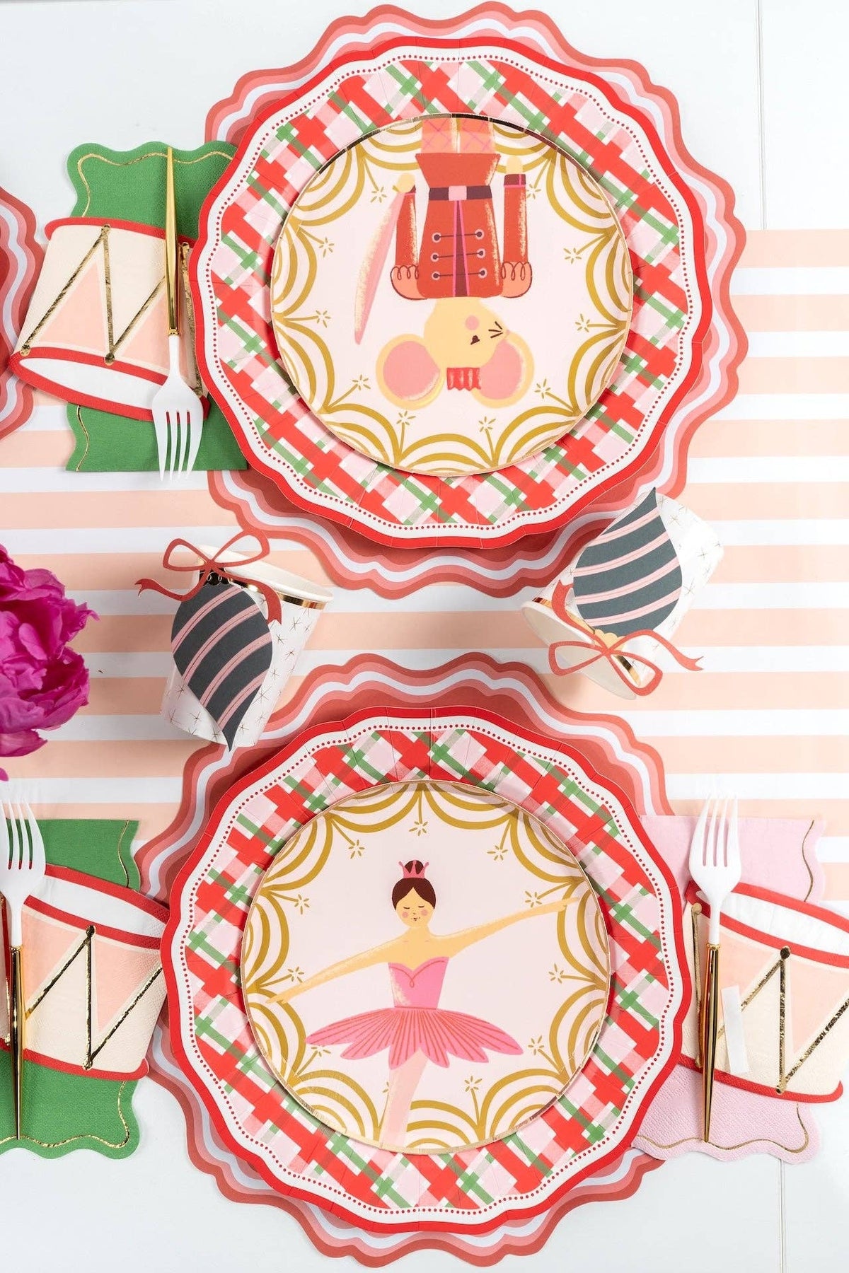 Overhead of nutcracker and ballerina plates on plaid plates with a striped ornament and a red drum napkin.