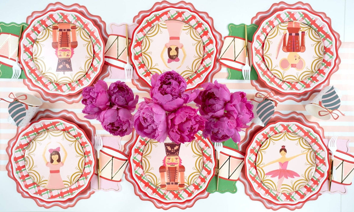 Overhead of pink nutcracker and drum plates on plaid plates around a bunch of pink peonies.