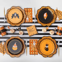 Orange argyle Happy Halloween paper napkins with scalloped edges between vintage Halloween character plates on a black and white striped runner