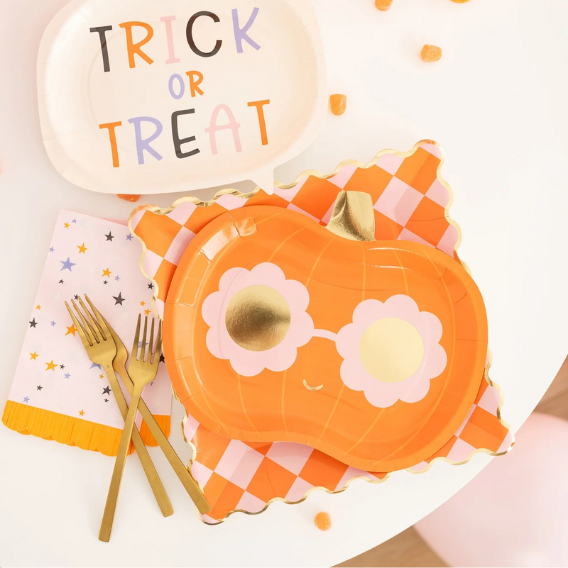 Halloween-themed table setting with a pumpkin plate, 'Trick or Treat' sign, and gold forks.