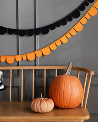 Decorative Halloween setup with pumpkins and a black and orange felt banner on a wooden surface.