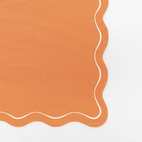 Single folded orange paper guest towel showing the pumpkin color and wavy scalloped edge up close.