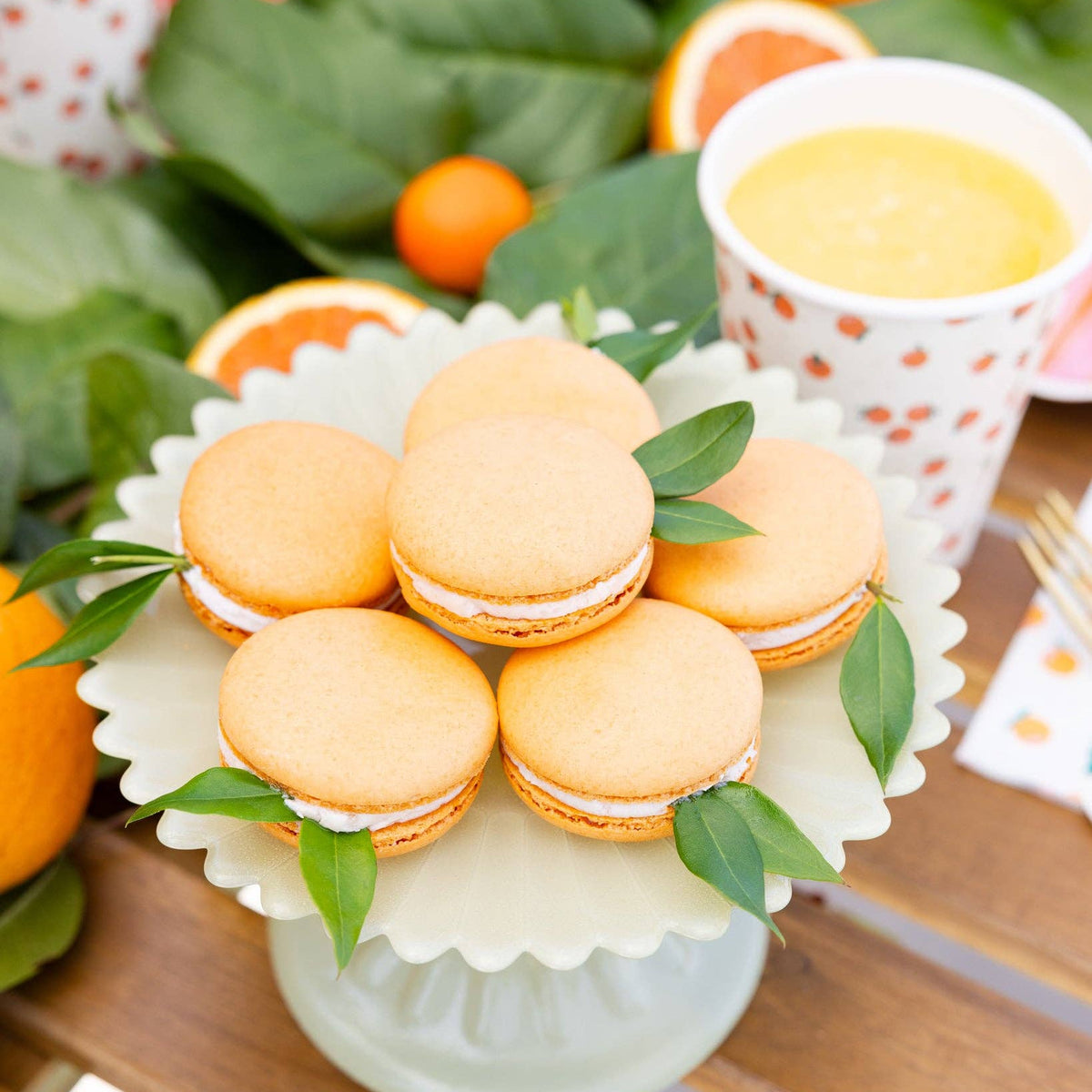 Orange macarons displayed beside matching orange party cups and citrus decor.