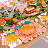 Orange cocktail napkin beside citrus desserts and gold party flatware.
