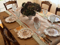 Orange plaid paper napkins with a scalloped edge layered under pumpkin napkins and flatware along a gingham floral table runner with turkey plates